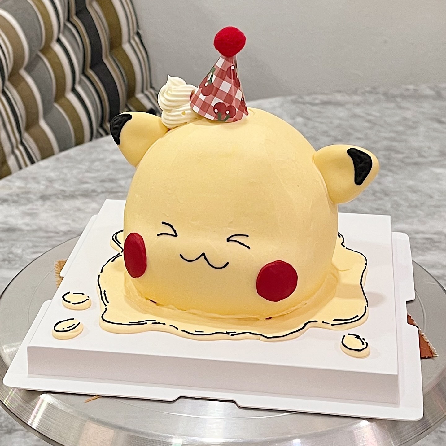 Yellow round-eared character cake with a party hat on a melting-drip board