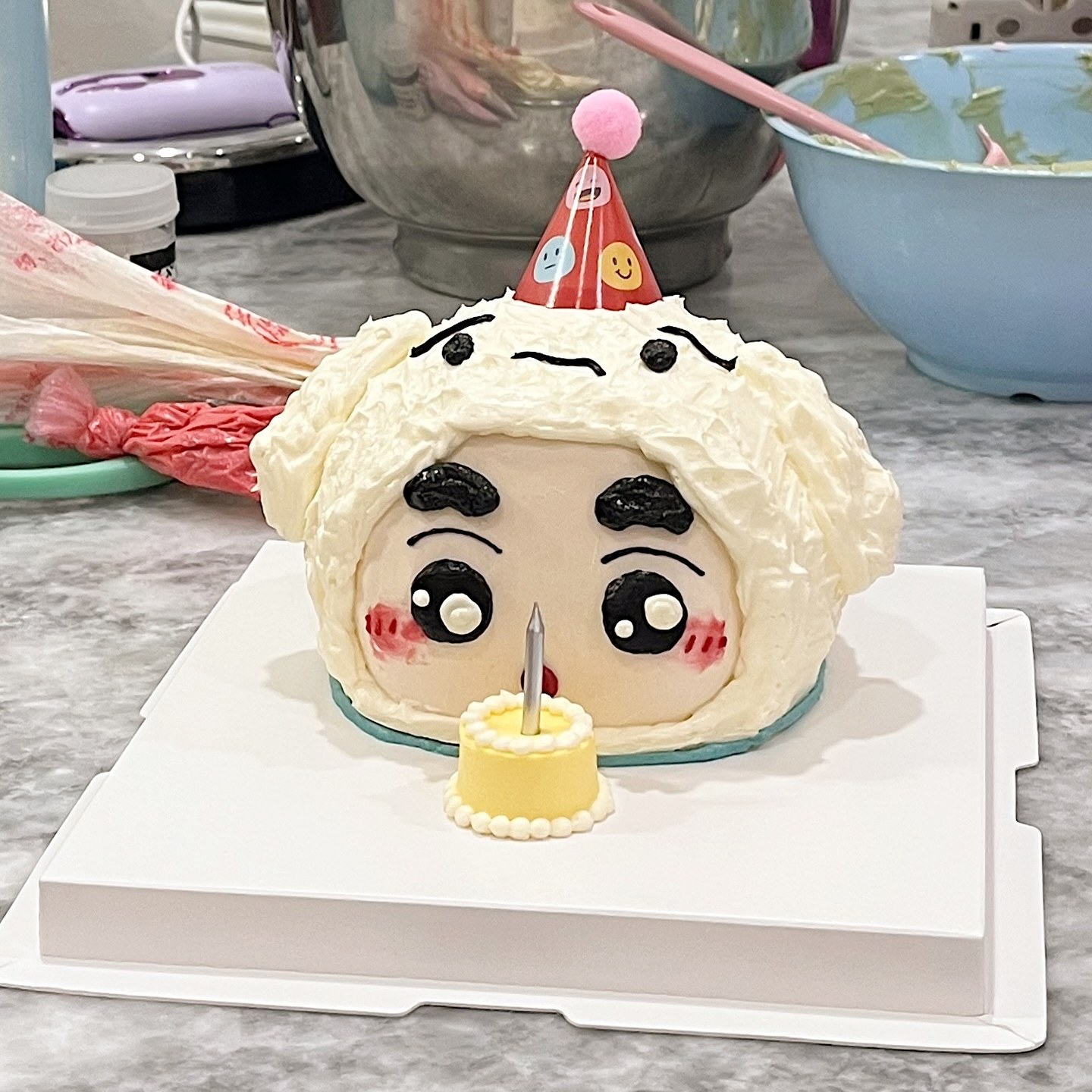 Fluffy white character cake with a party hat and a mini candle cake