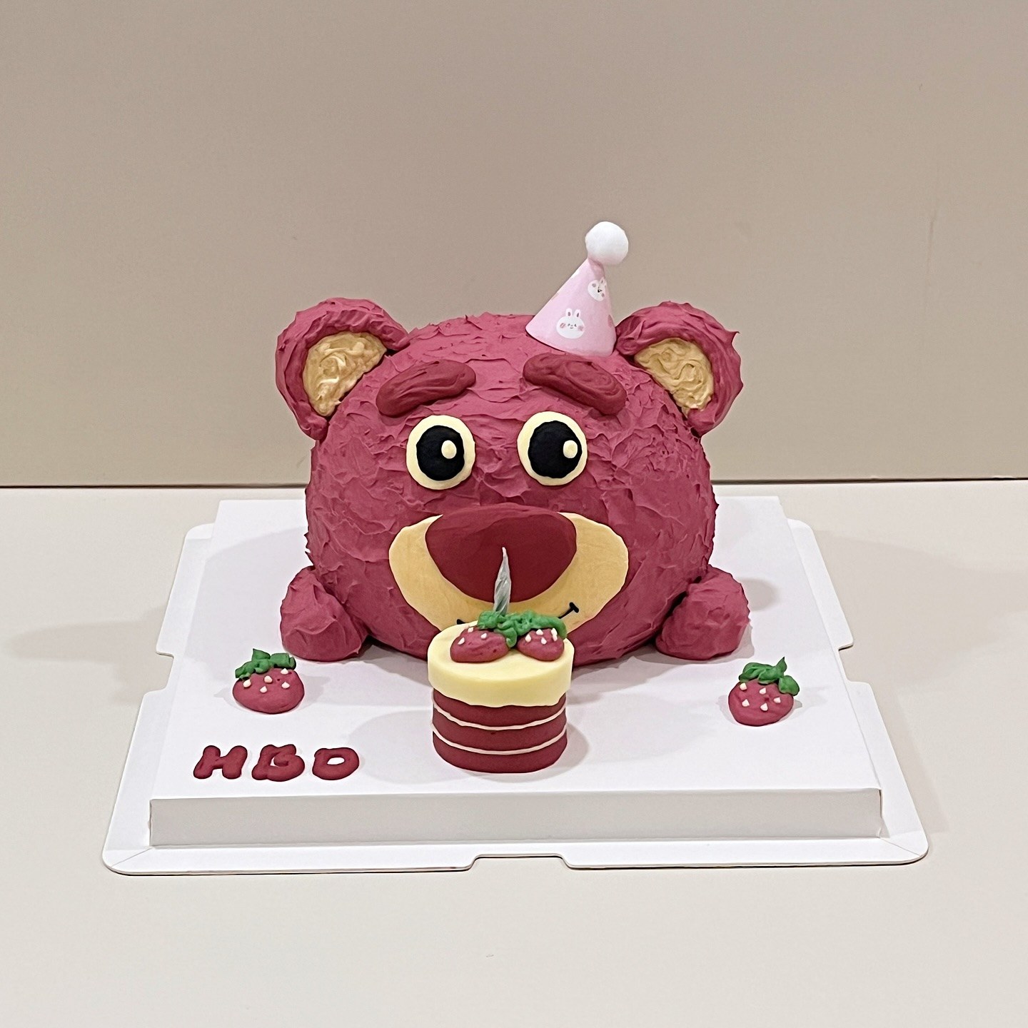 Pink bear character cake with a party hat and a mini strawberry cake
