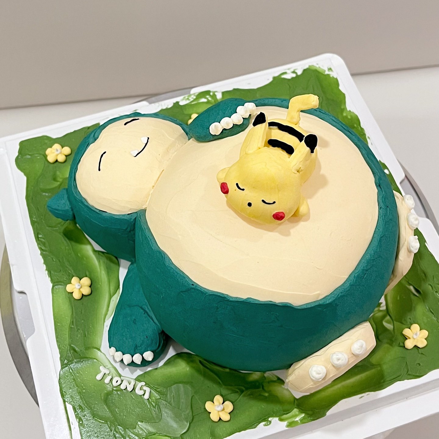 Sleepy green character cake with a small yellow companion cake on a grassy board
