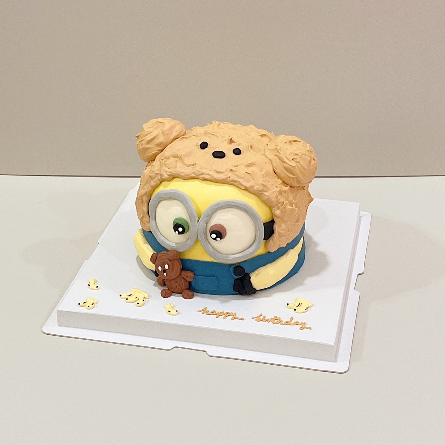 Fluffy character cake with round goggles and blue overalls, holding a mini teddy bear