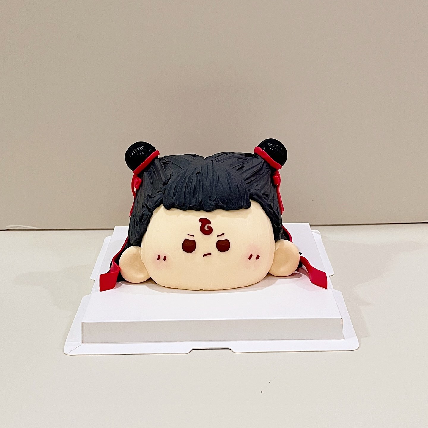 Chibi character cake with black hair buns, red ribbons and a fierce expression