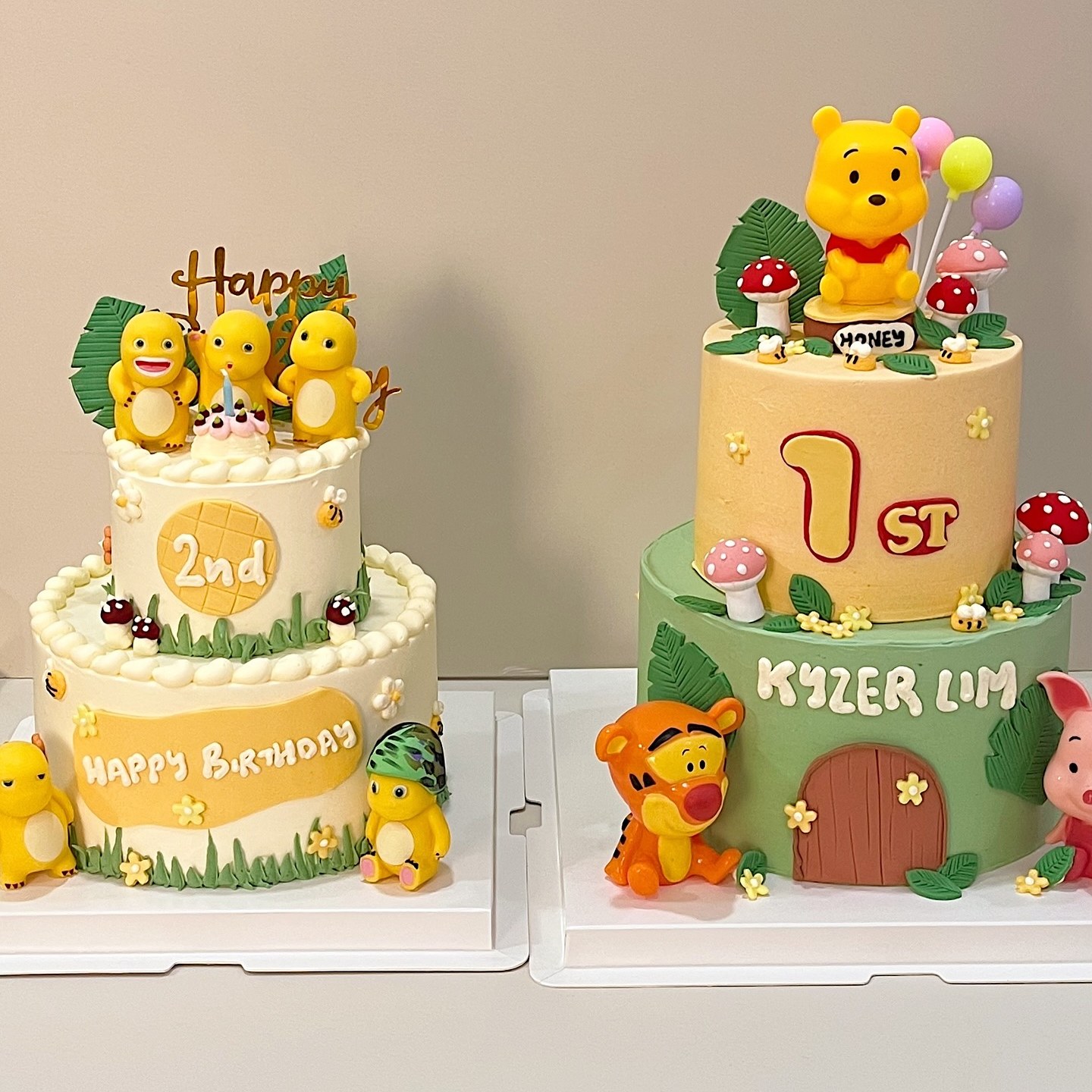 Two side-by-side cakes with honey-pot bear and friends figurines, mushrooms and jungle leaves