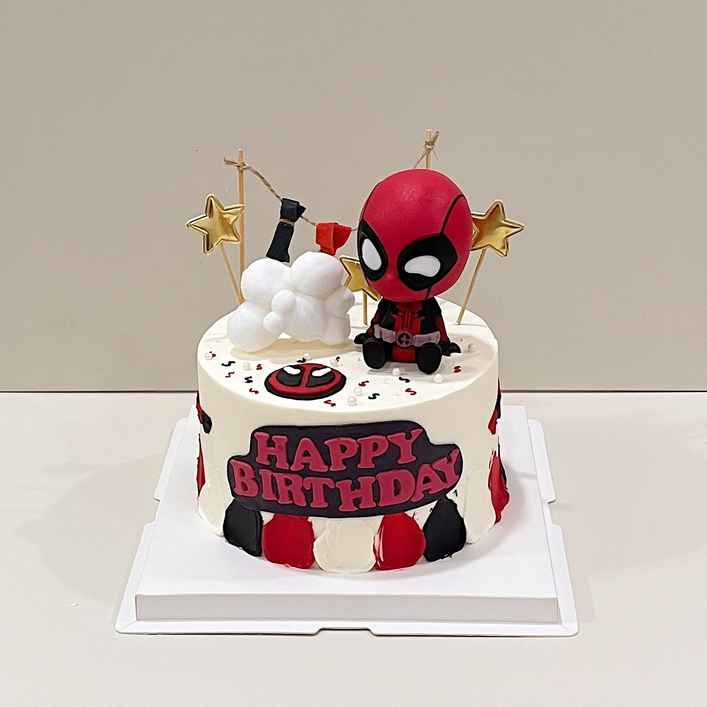 White cake with a superhero figurine, gold stars and a Happy Birthday topper