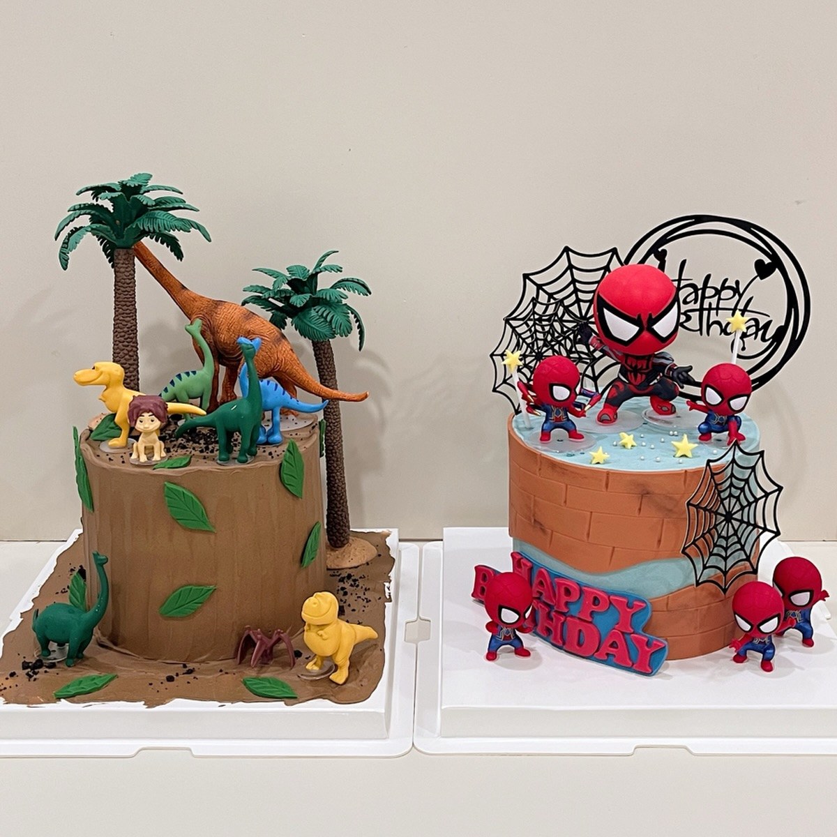 Dinosaur-themed cake and a superhero-themed cake with toy figurines, side by side