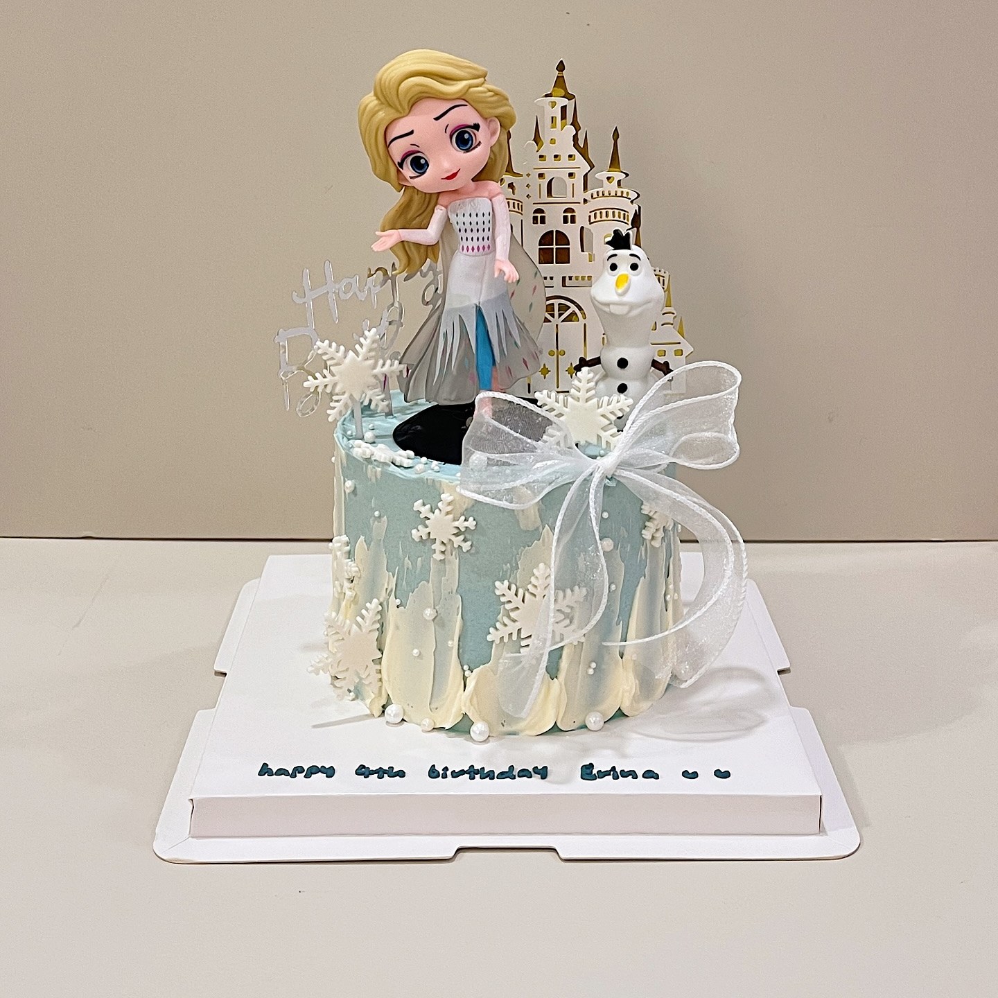 Winter-themed cake with snowflakes, a bow, and princess and snowman figurines