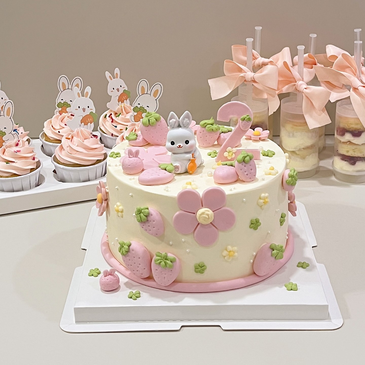 Pastel cake with a bunny figurine, strawberries and florals, with matching cupcakes