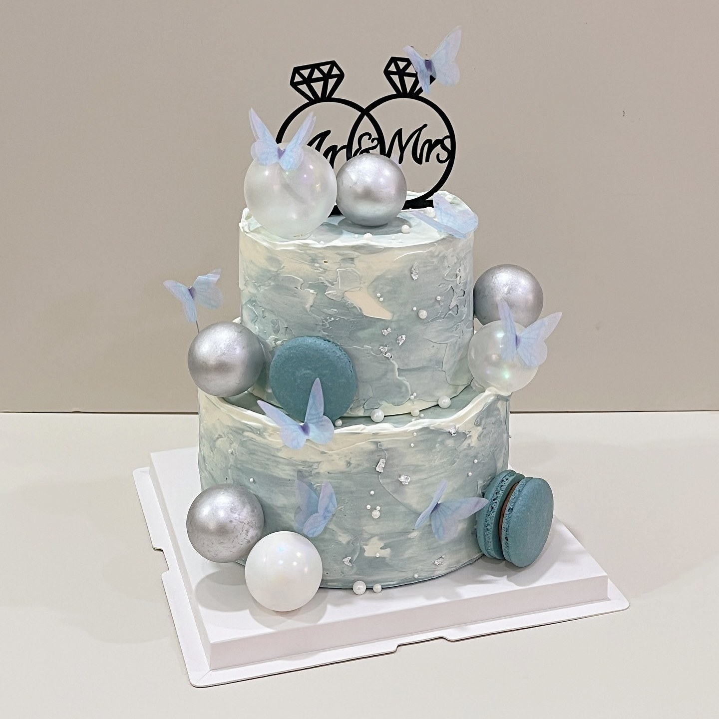 Two-tier marbled cake with macarons, silver spheres and butterflies, topped with a Mr and Mrs sign