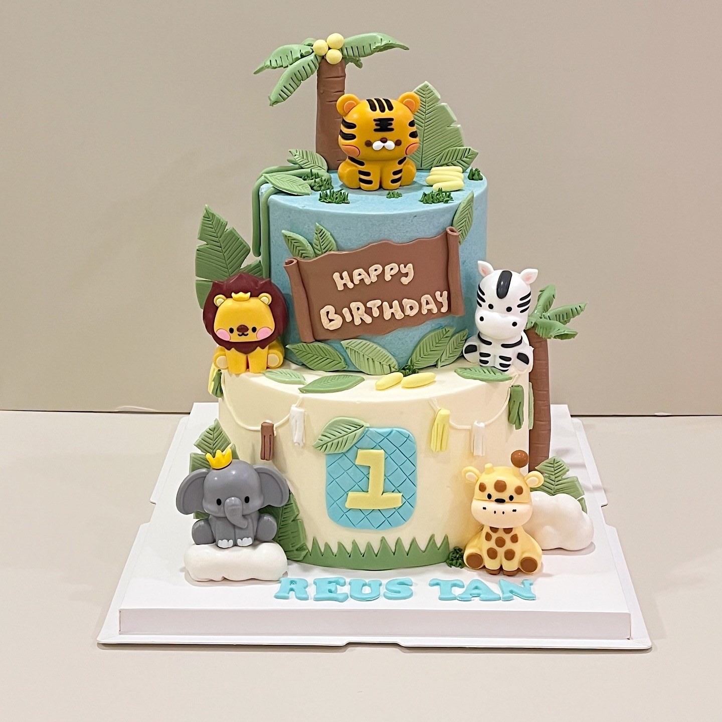 Two-tier jungle animal-themed cake with lion, tiger, zebra, elephant and giraffe figurines