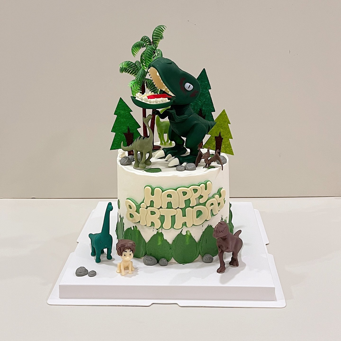 Dinosaur-themed birthday cake with toy dinosaur figurines and palm trees