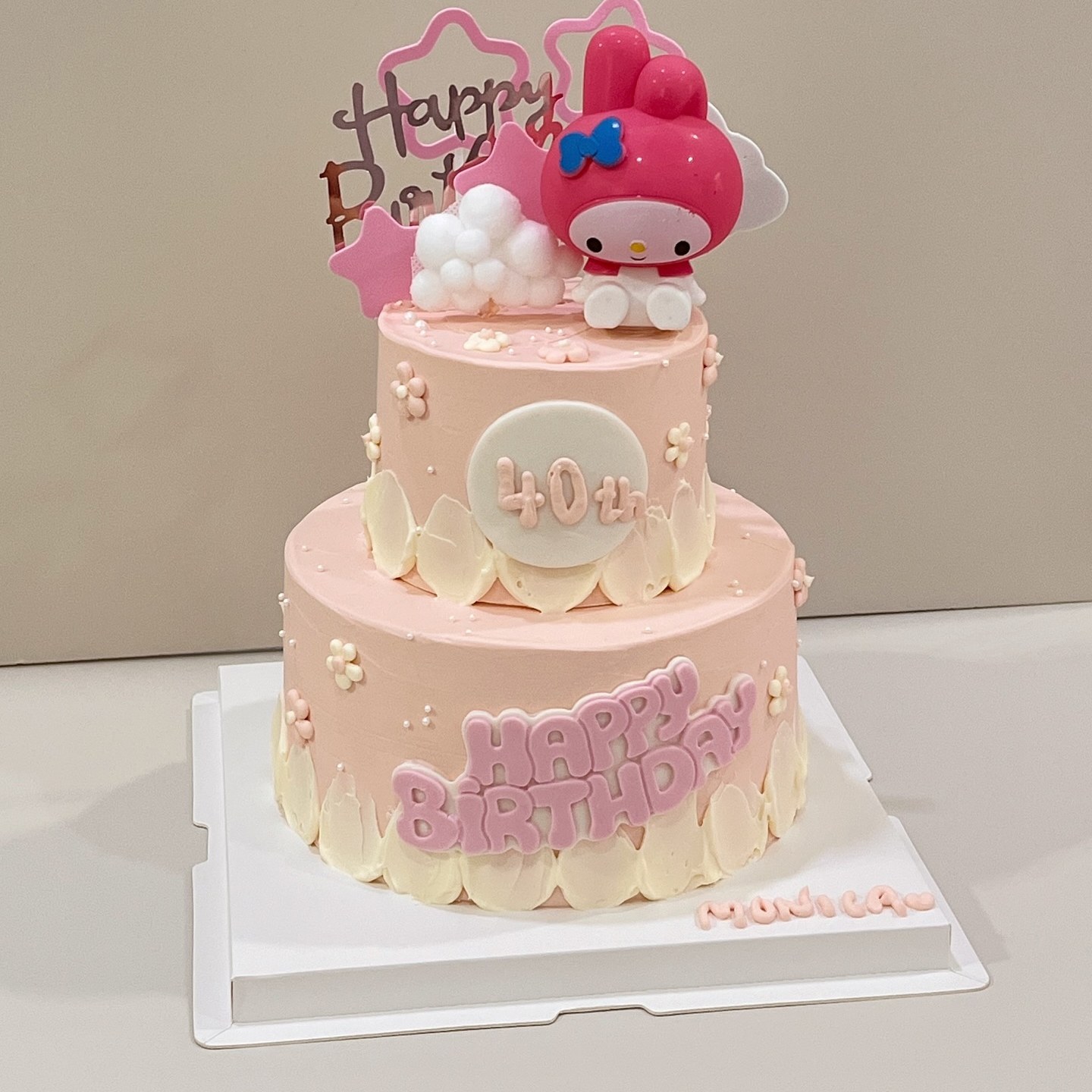 Two-tier pink cake with a bunny character figurine and floral piping